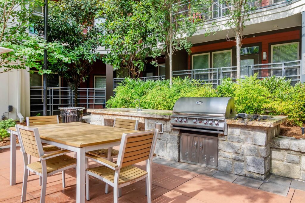 Outdoor area with grill, tables and chair. Residential building in the back