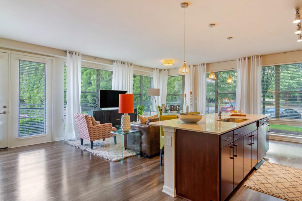 Living room surrounded by windows, with wood floor and kitchen island