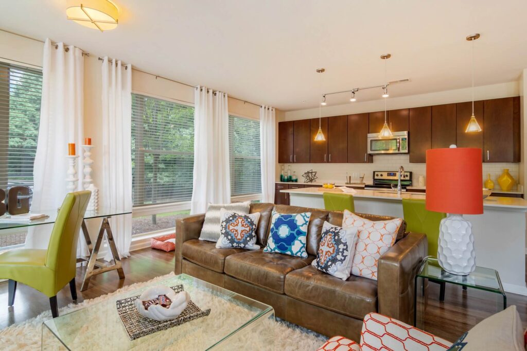 Living room with wood floors with kitchen in the back with stainless steal appliances and wall of windows
