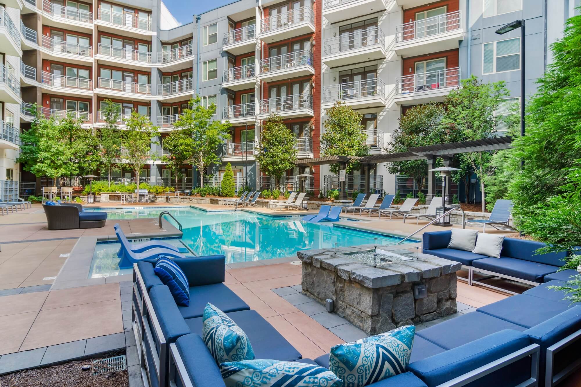 Community pool area with lounge chairs, in pool seating, and fire pit with sectional surrounding.