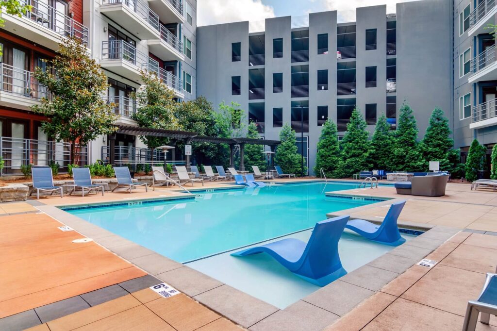 Pool area with in pool seating and lounge chairs. Residential building and parking garage in the background.