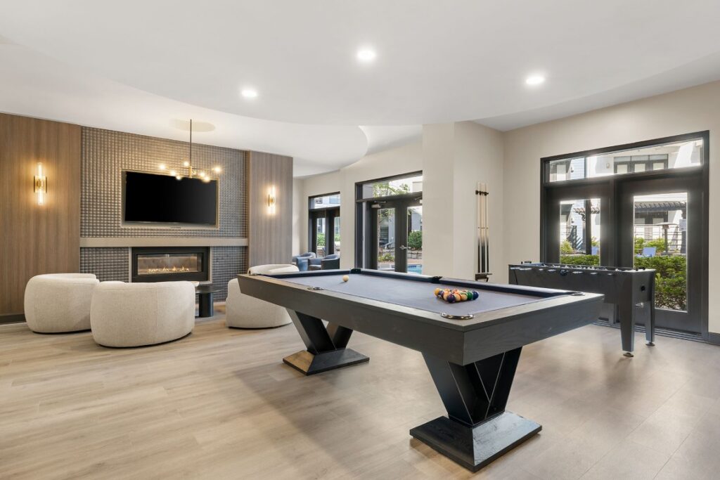 A lounge area featuring a pool table, a foosball table, and a seating area with a fireplace and television.