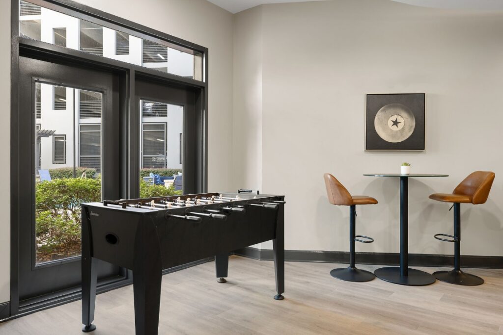 A foosball table sits in a room with a small round cafe table, two stools, and a piece of circular star-themed wall art.