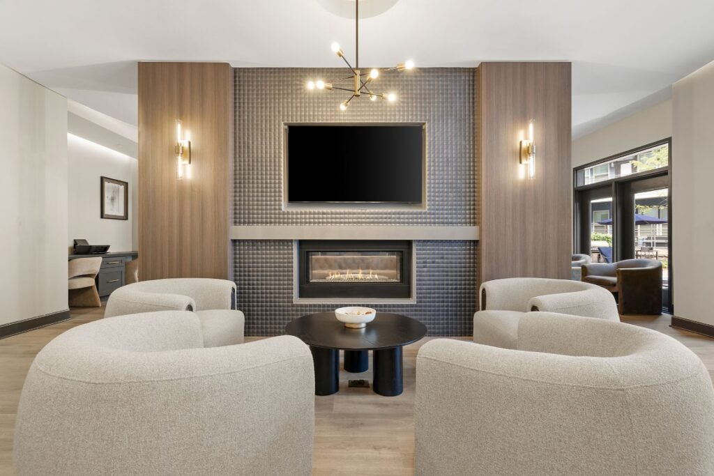 Four curved armchairs arranged around a round coffee table in front of a fireplace with a mounted television above.
