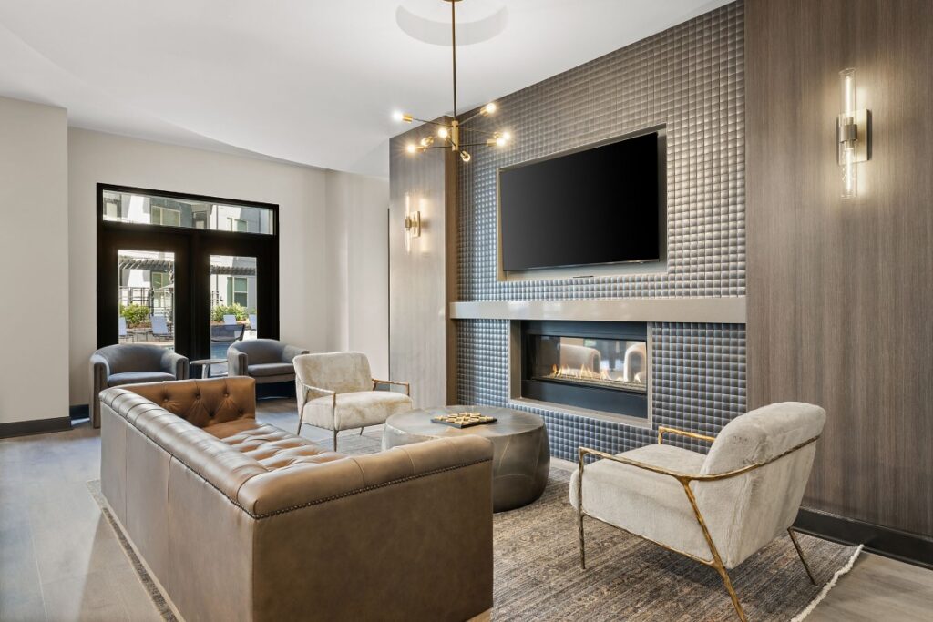 A modern lounge featuring a tufted leather sofa, two armchairs, a coffee table with a game board, and a television mounted above a fireplace.