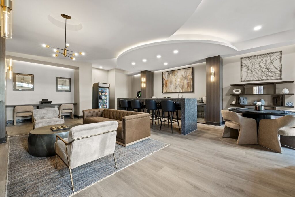 Modern lounge area with a brown leather sofa, armchairs, a kitchen island with bar stools, and a small dining table.