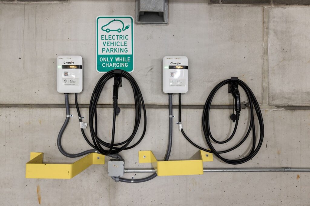 Two electric vehicle charging stations mounted on a concrete wall below an Electric Vehicle Parking Only While Charging sign.