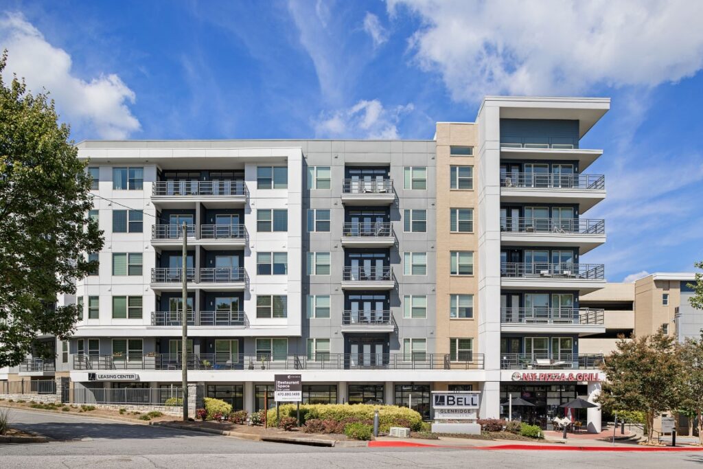A modern multi-story apartment building with a ground-floor retail space, featuring a leasing center, a restaurant, and a sign for Bell Glenridge.
