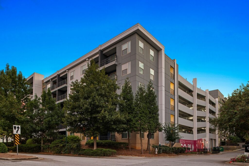 A multi-story modern apartment building with an integrated parking garage and surrounding trees.