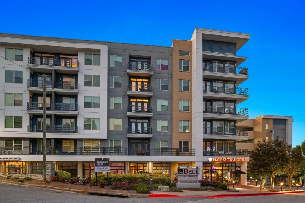 Modern multi-story apartment building with a street-level N.Y. Pizza & Grill restaurant, a leasing office, and a vacant restaurant space for lease.