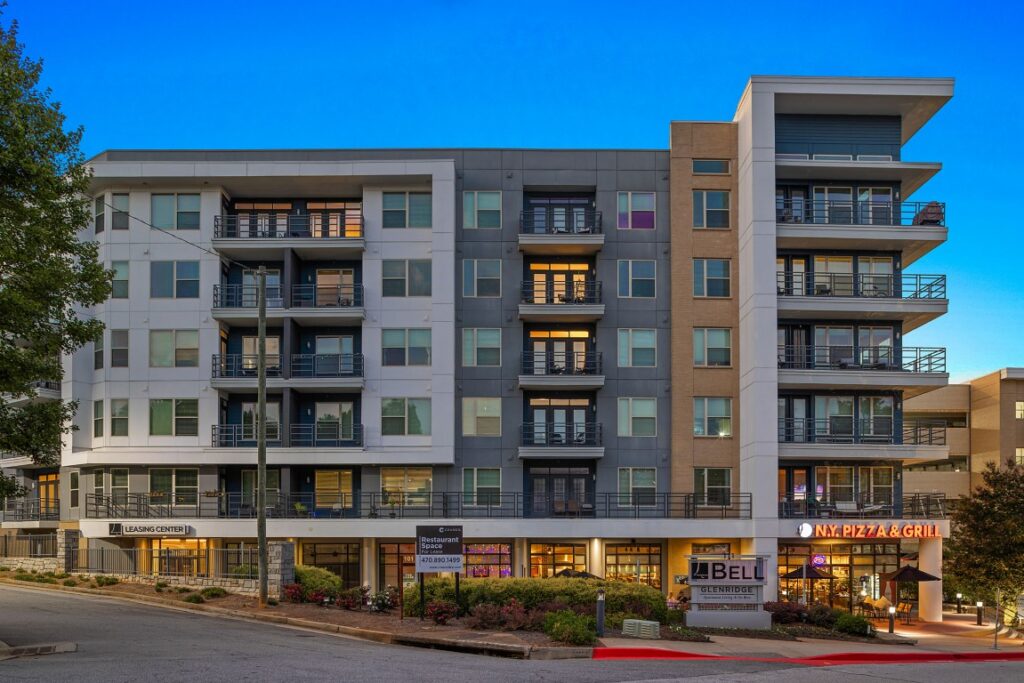 Multi-story apartment building with balconies, a leasing center, and a ground-floor pizza restaurant at dusk.