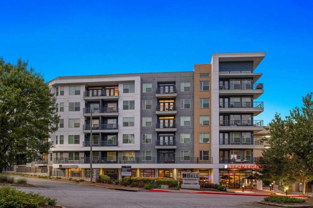 Exterior view of a multi-story apartment complex at dusk with ground-level retail spaces for Bell Glenridge and N.Y. Pizza & Grill.