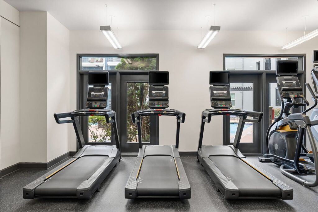 Three treadmills lined up in a gym, with a partial view of an elliptical machine on the right.