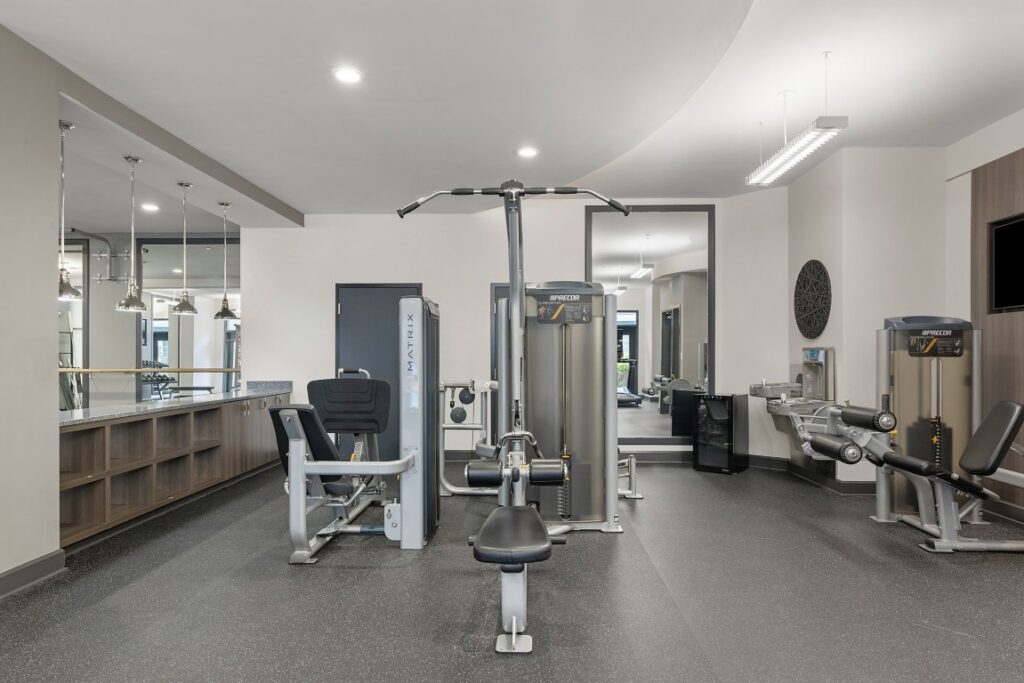 A fitness center containing several strength training machines, a water cooler, and a counter with cabinets.