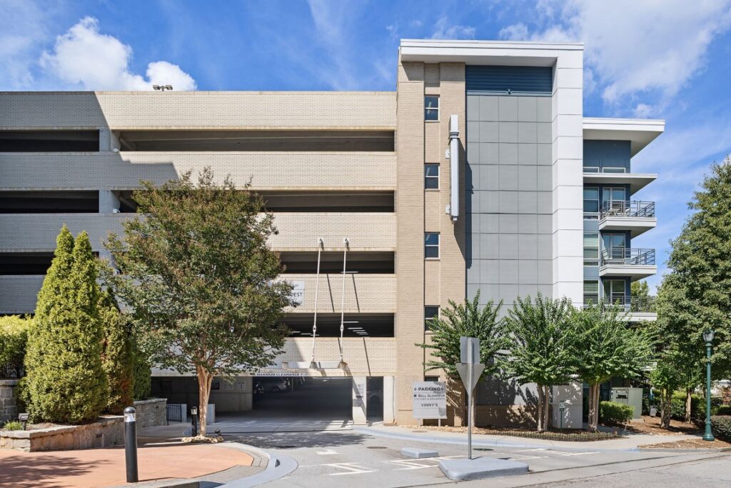 A multi-level parking garage entrance with a sign for Bell Quarters, featuring a tan brick exterior and a section of modern apartment balconies.