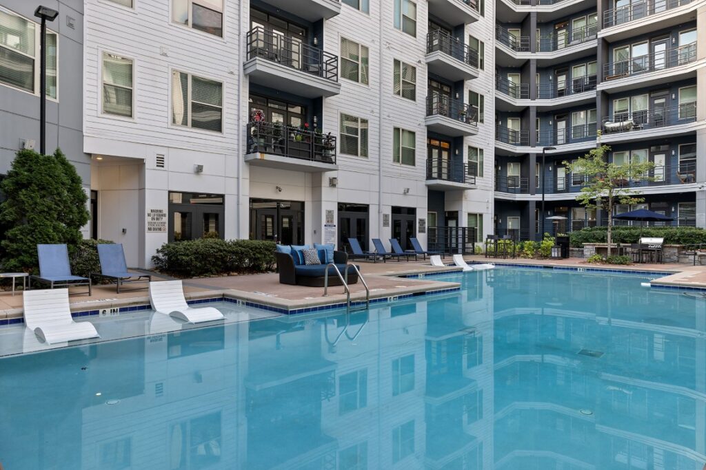 A swimming pool in a courtyard surrounded by the white and dark gray exterior of a modern multi-story apartment building.