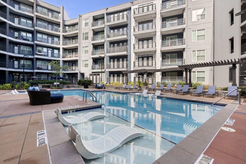 Courtyard swimming pool at an apartment complex with in-pool lounge chairs and surrounding patio seating.