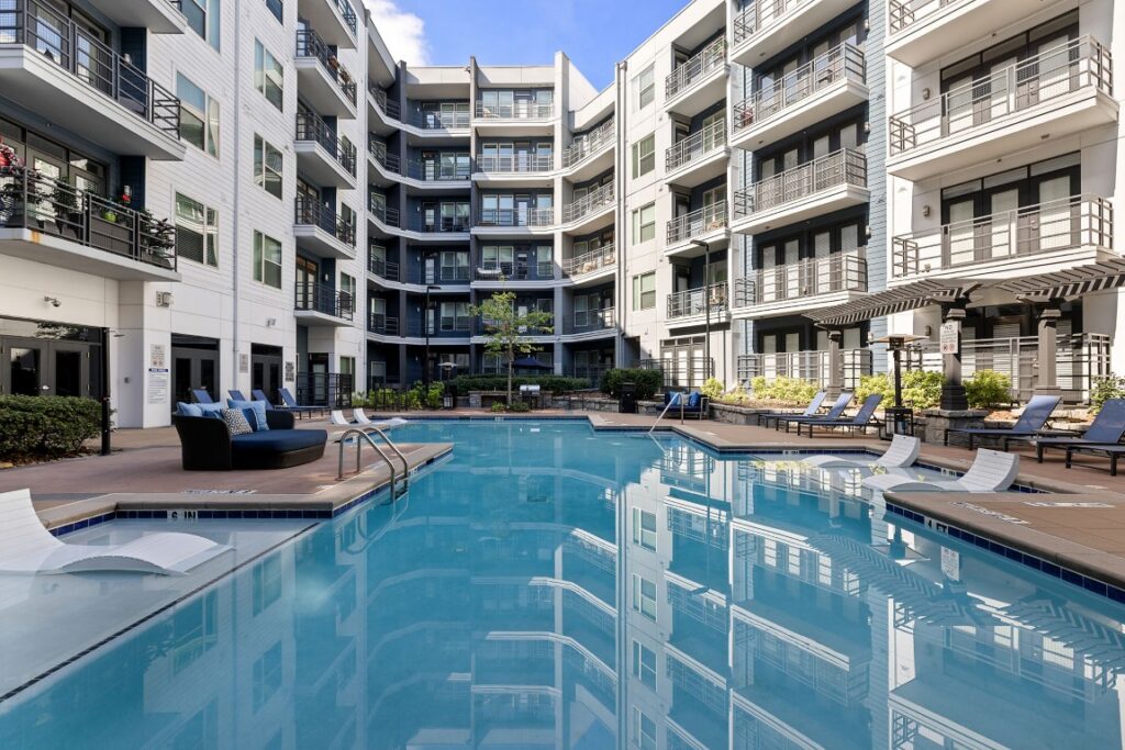 U-shaped apartment building surrounding a central swimming pool with lounge chairs on the deck.