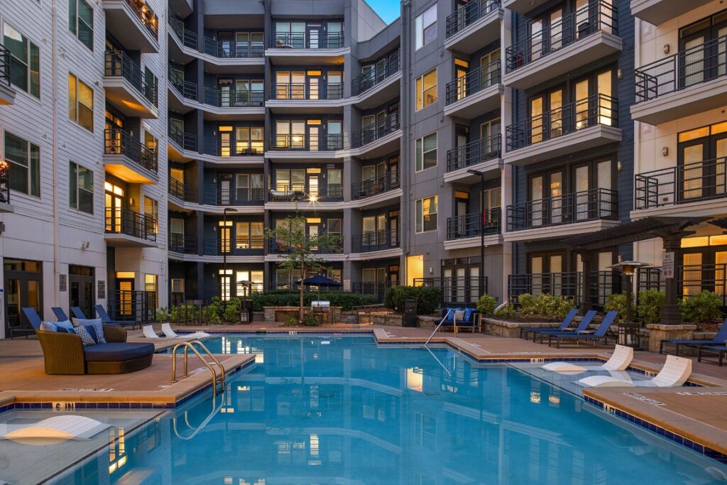 Swimming pool in the courtyard of a multi-story apartment complex with balcony railings and lounge chairs.