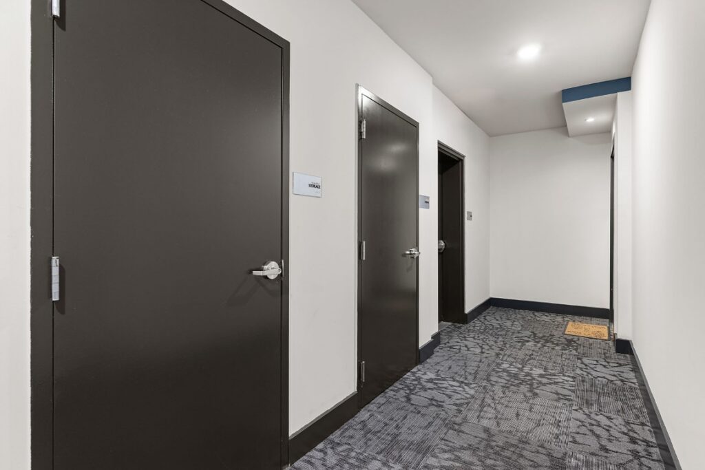 A hallway with gray patterned carpeting featuring three dark doors and white walls.