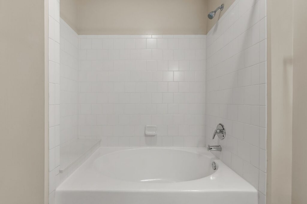 A white bathtub with a shower head and a tiled surround.