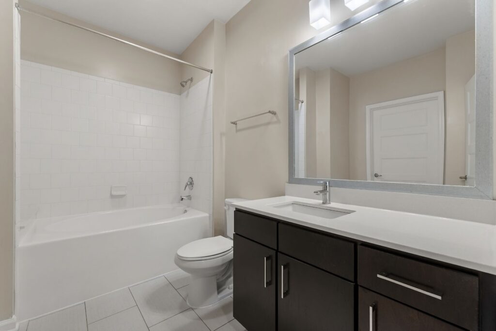 Bathroom with a white bathtub and shower surround, a toilet, and a dark wood vanity with a white countertop and large mirror.