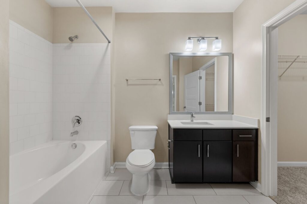 A bathroom with a white bathtub, toilet, and a vanity with a dark wood cabinet and a rectangular mirror.