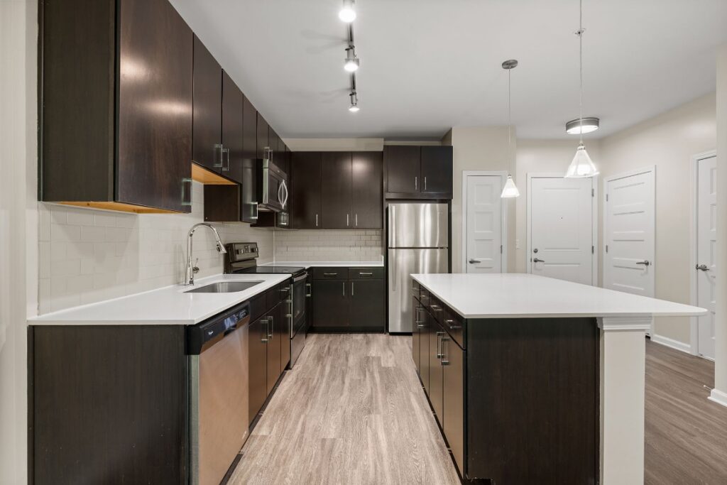 Modern kitchen with dark wood cabinets, white countertops, stainless steel appliances, and a central island.