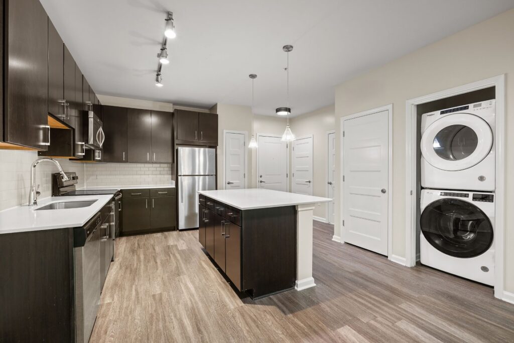Modern kitchen with dark wood cabinets, white countertops, a center island, and a stacked washer and dryer unit in a wall alcove.