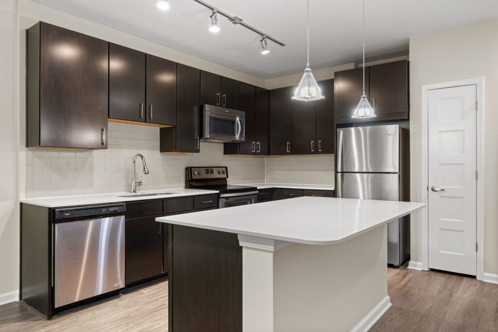 Modern kitchen with dark wood cabinets, white countertops, stainless steel appliances, and a central island.