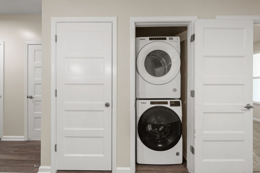 Stacked white Whirlpool washer and dryer in a laundry closet between two closed white doors.